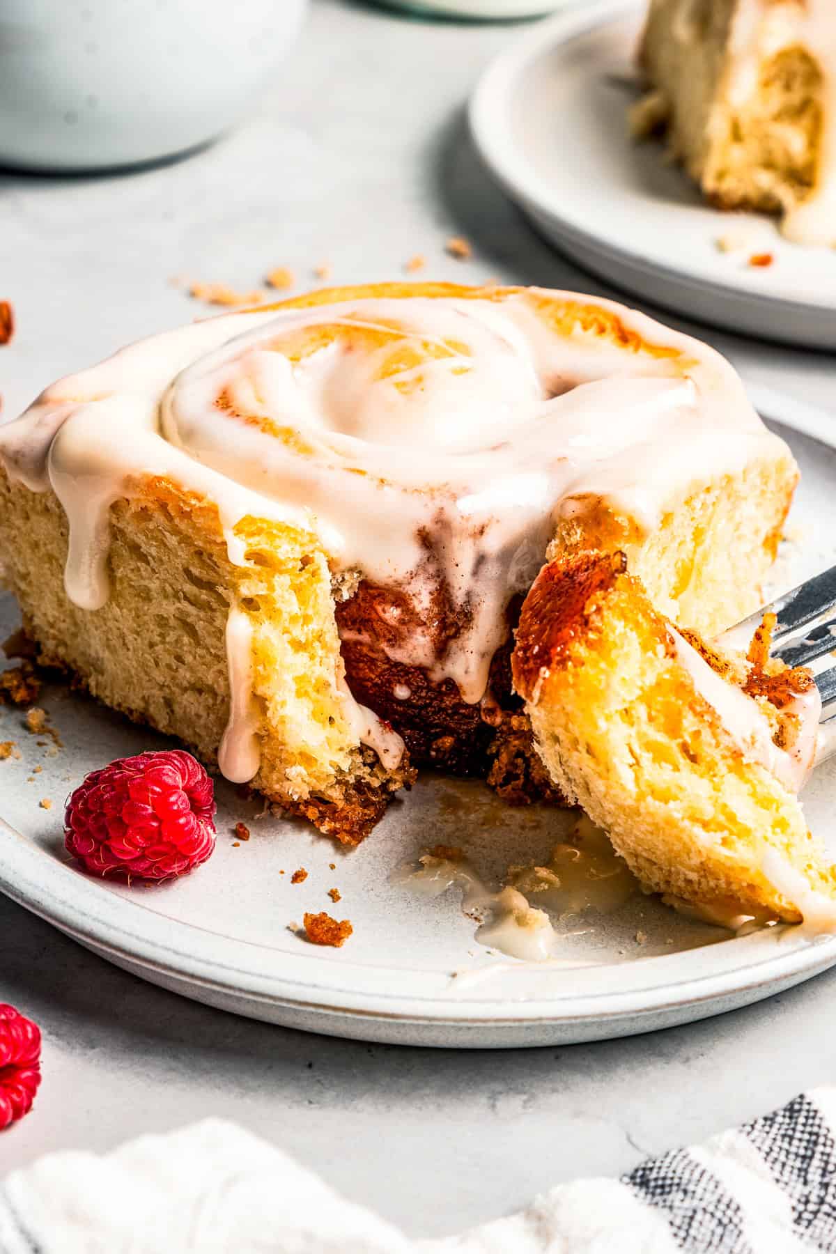 This cinnamon roll recipe makes big, bakery-style cinnamon buns filled with gooey cinnamon sugar and topped with sweet cream cheese frosting. A cinnamon roll with a forkful missing on a plate.