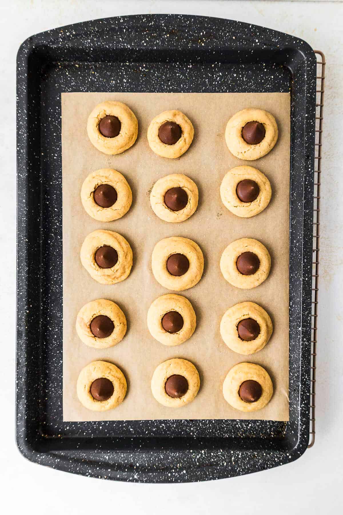 This peanut butter blossoms recipe makes soft, thick peanut butter cookies topped with a chocolate kiss. Easy to make and perfect for any occasion. Peanut butter blossom cookies on a baking sheet.