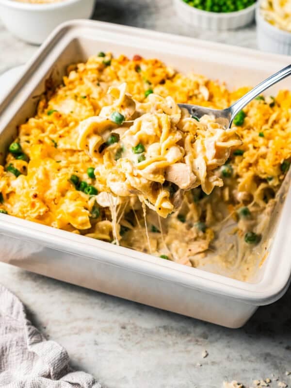 A serving spoon scooping tuna noodle casserole from a square baking dish.