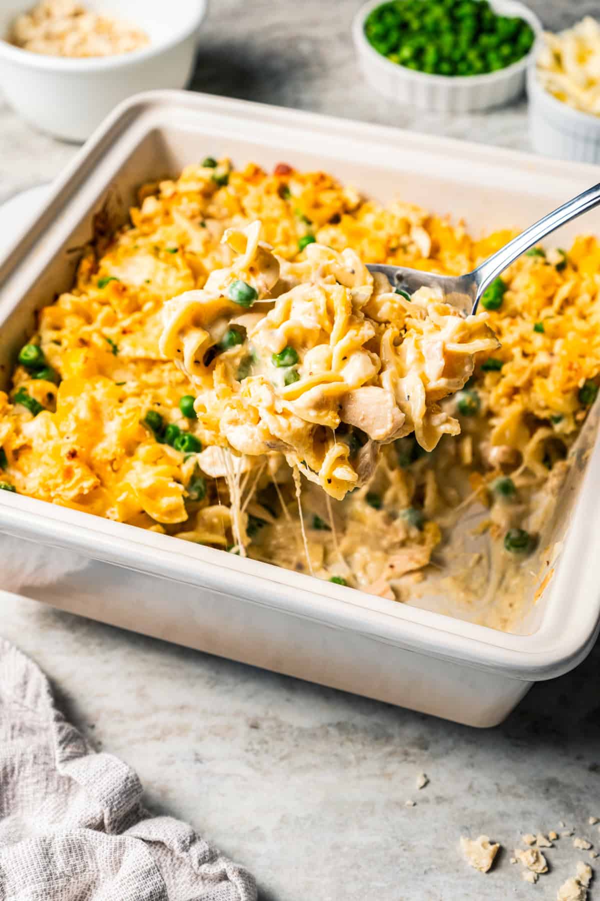 A serving spoon scooping tuna noodle casserole from a square baking dish.