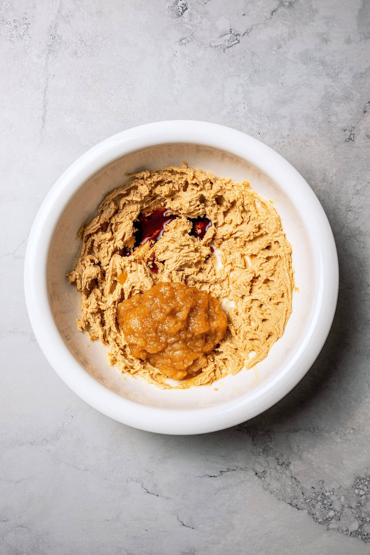 These moist applesauce muffins are easy to make and are packed with brown sugar and cinnamon, topped with extra sugar for a crunchy finish! Applesauce added to muffin batter ingredients in a bowl.