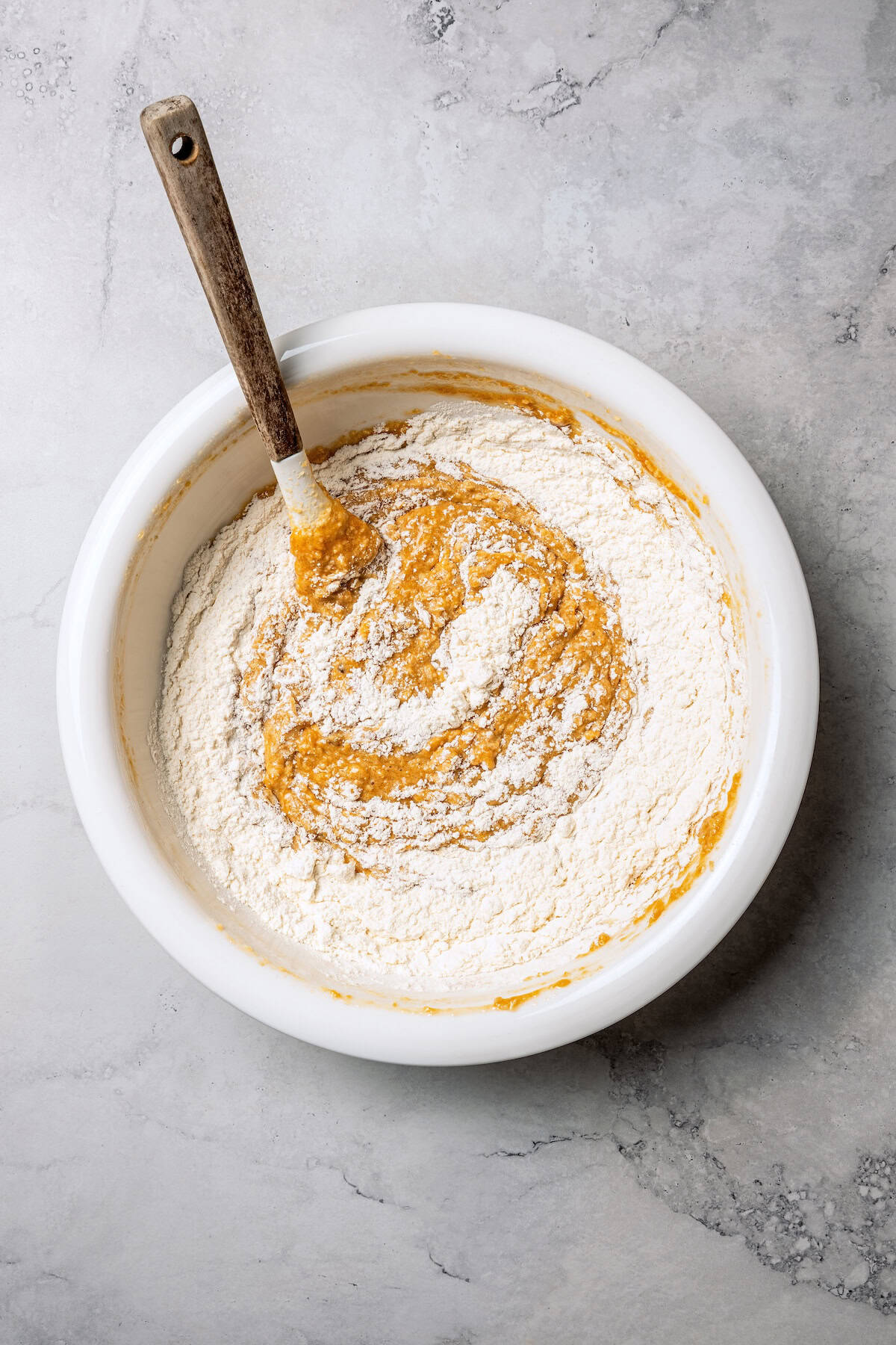 These moist applesauce muffins are easy to make and are packed with brown sugar and cinnamon, topped with extra sugar for a crunchy finish! Dry ingredients partially stirred into the wet muffin batter in a bowl.