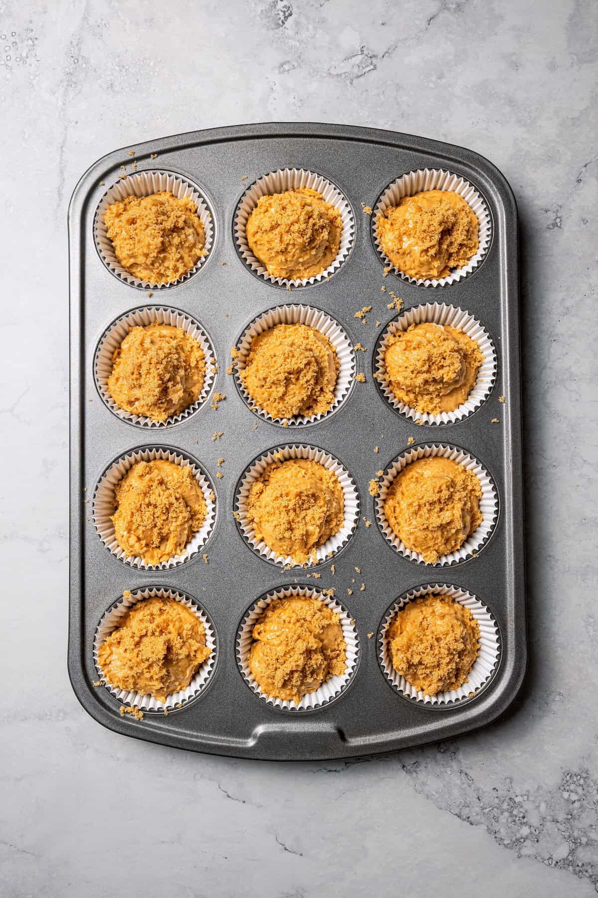 These moist applesauce muffins are easy to make and are packed with brown sugar and cinnamon, topped with extra sugar for a crunchy finish! A lined muffin pan filled with applesauce muffin batter.