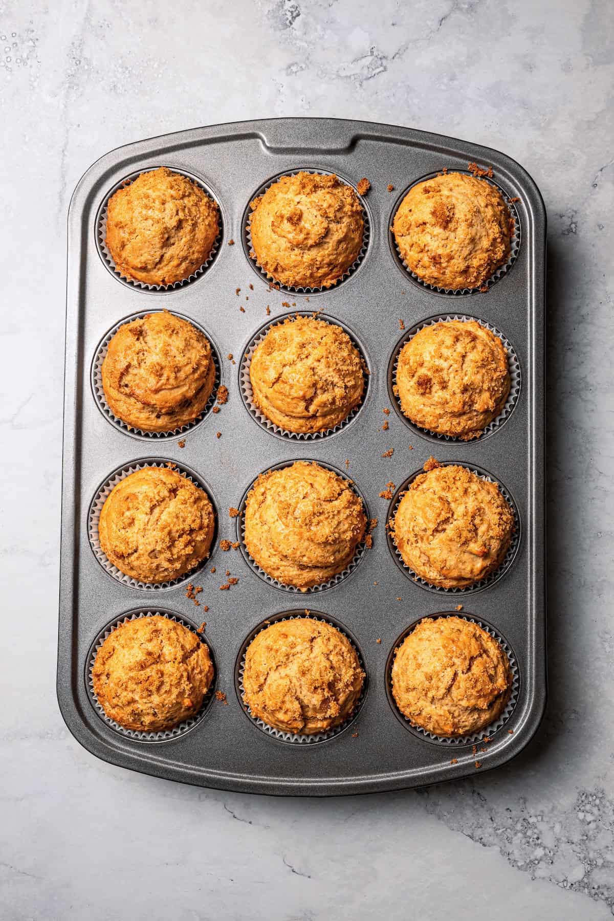 These moist applesauce muffins are easy to make and are packed with brown sugar and cinnamon, topped with extra sugar for a crunchy finish! Overhead view of freshly baked applesauce muffins in a 12-well muffin pan.