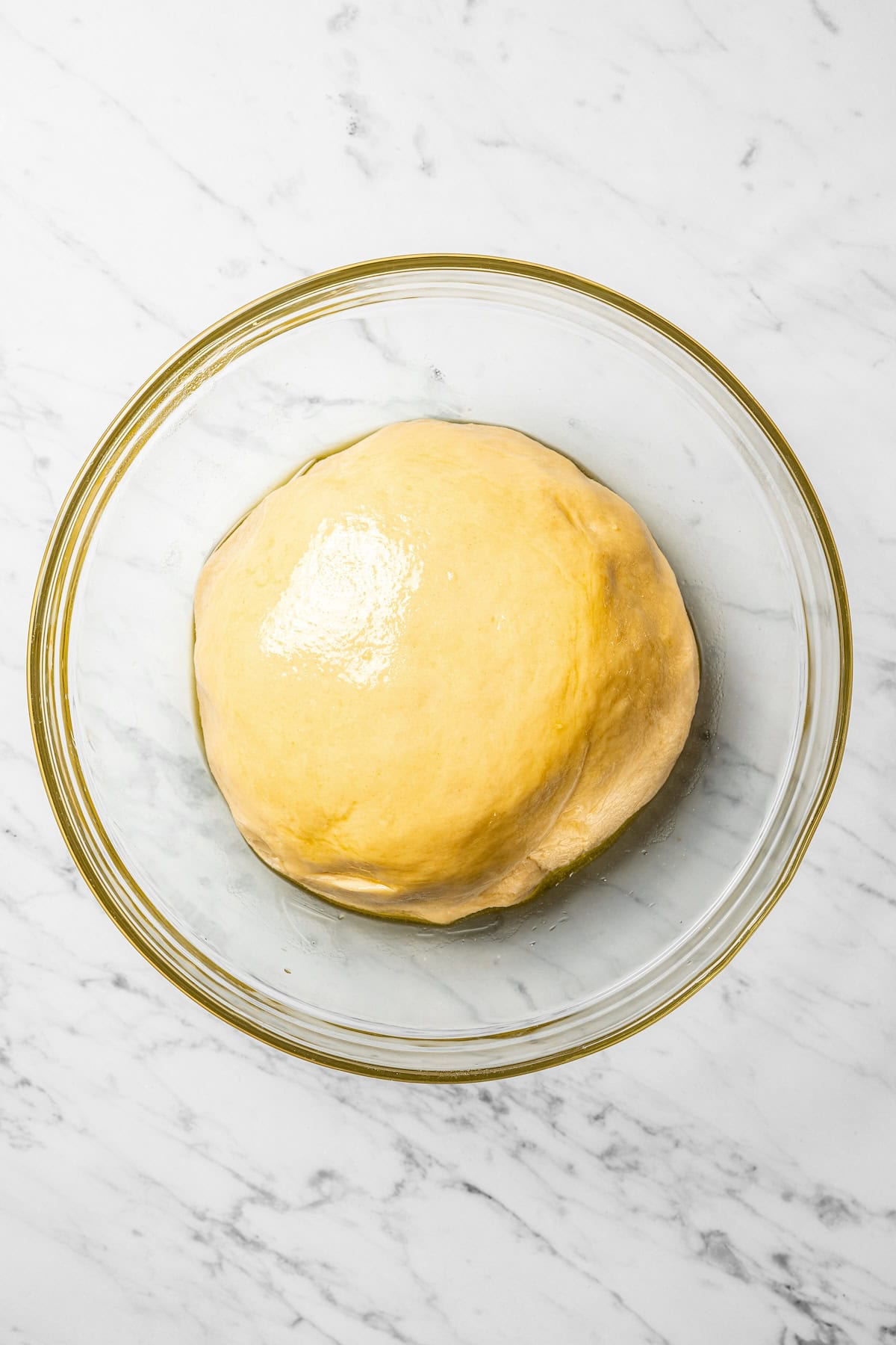 A round, glossy ball of dough left to rise in a glass bowl.