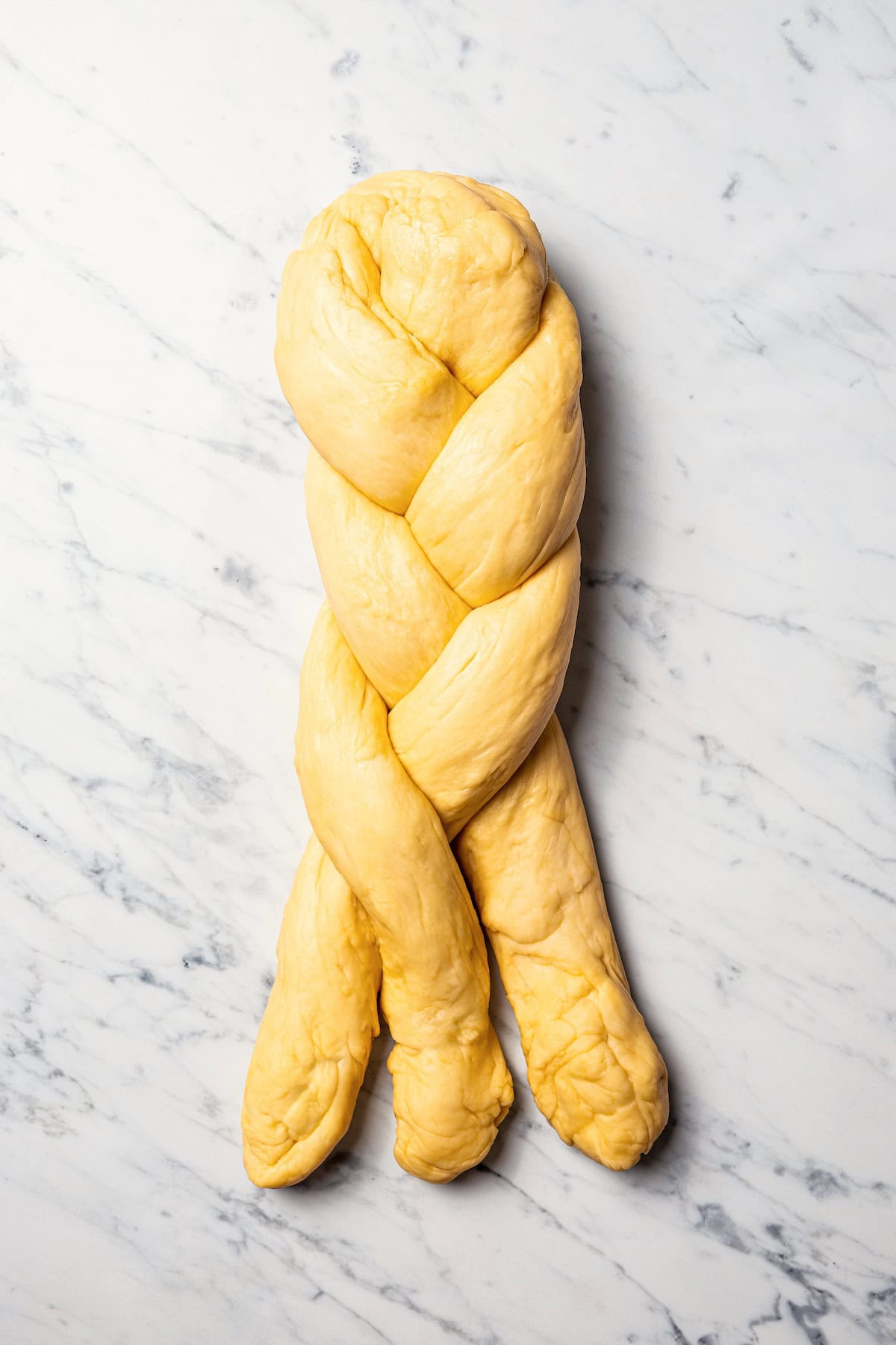 Challah dough ropes partially braided on a countertop.