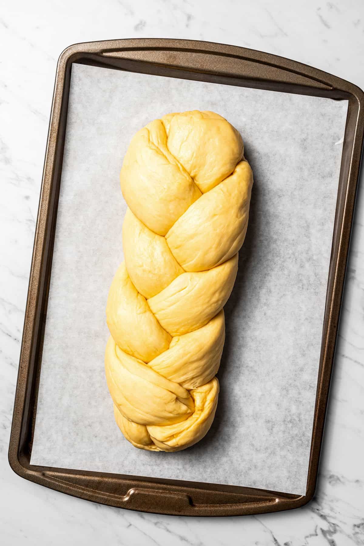 Braided challah dough on a parchment-lined baking sheet.
