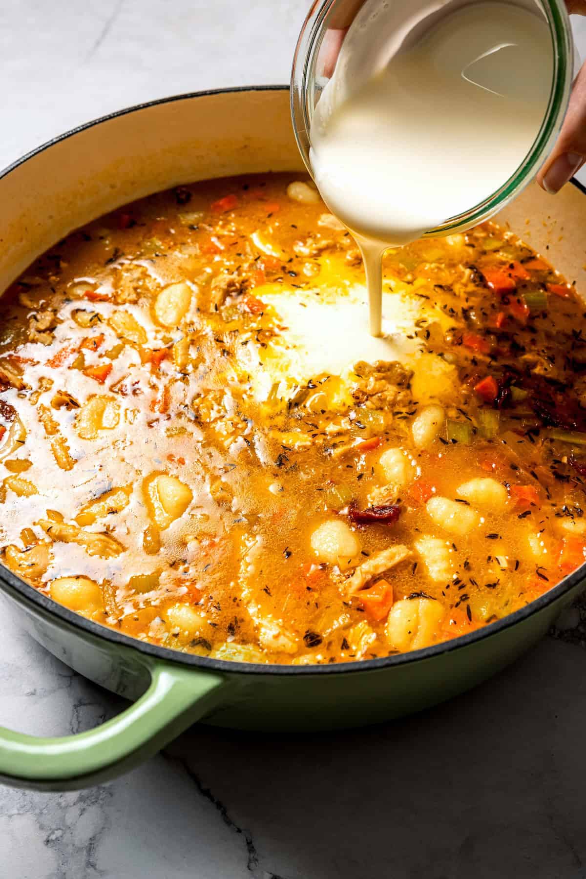 This chicken gnocchi soup is even better than the Olive Garden! It's ready in 20 minutes, extra creamy, and packed with flavorful ingredients. Heavy cream being added to a pot of chicken gnocchi soup.
