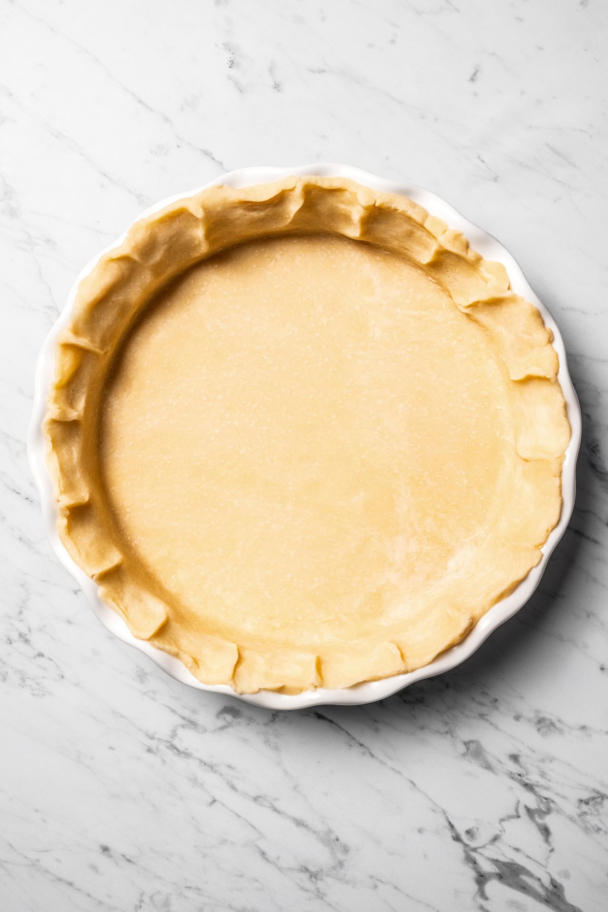 This easy coconut cream pie recipe features a thick, creamy coconut filling topped with fresh whipped cream in a golden, flaky pie crust. Pie crust pressed and shaped into a pie plate.