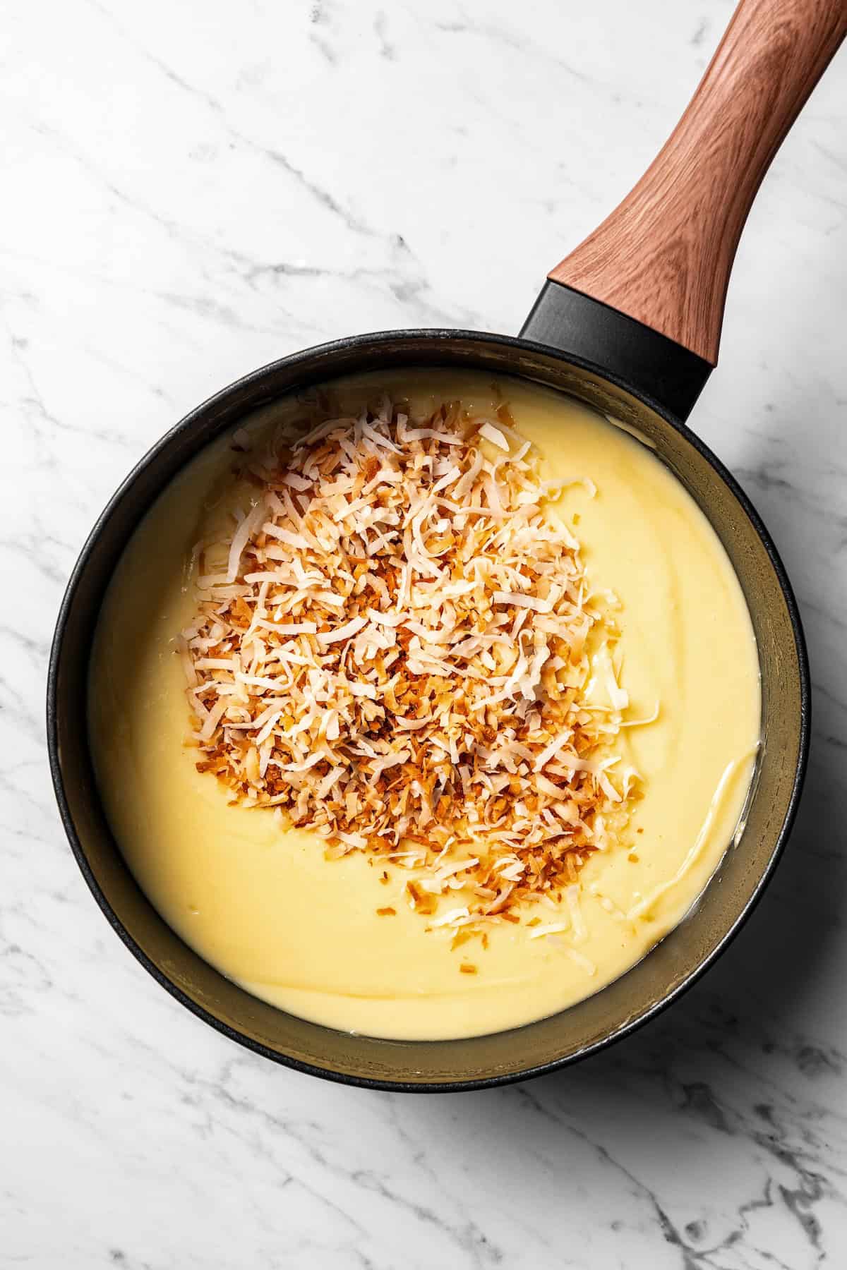 This easy coconut cream pie recipe features a thick, creamy coconut filling topped with fresh whipped cream in a golden, flaky pie crust. Toasted coconut added to the coconut cream filling in a saucepan.