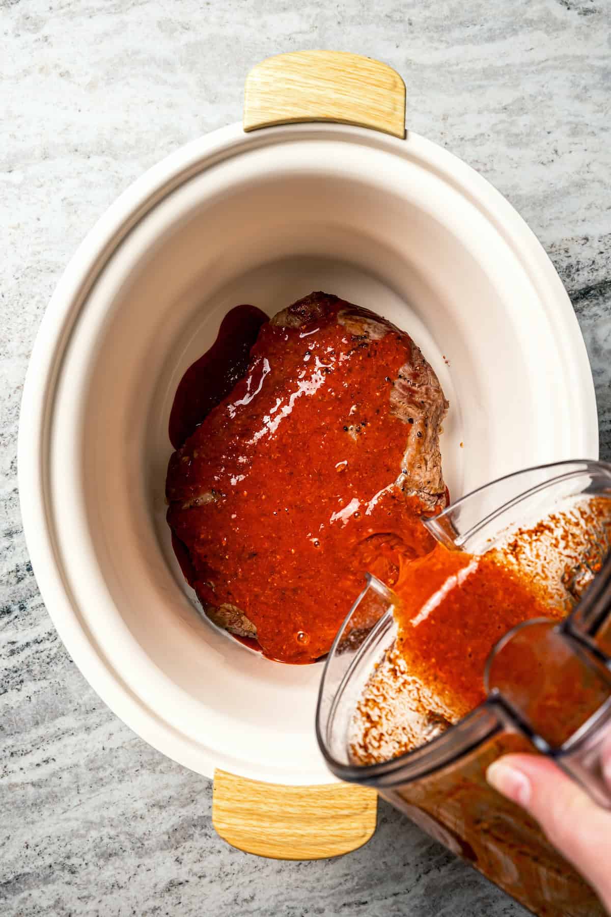 Crock pot carne asada has smoky spices and bright citrus, soaked into juicy shredded steak. Only 5 minutes to prep and perfect for tacos! Sauce being poured over flank steak for carne asada in the crock pot.