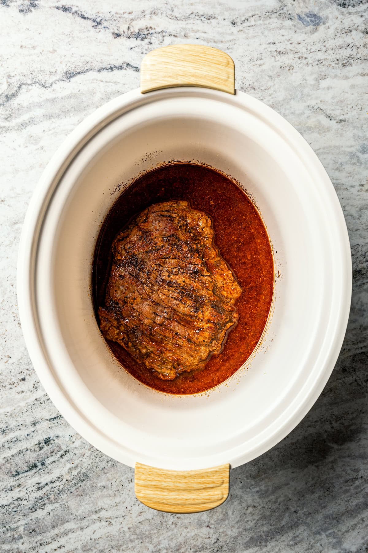 Crock pot carne asada has smoky spices and bright citrus, soaked into juicy shredded steak. Only 5 minutes to prep and perfect for tacos! Cooked flank steak for carne asada inside the crock pot.