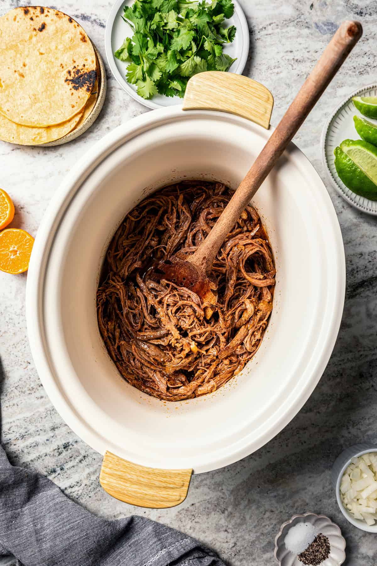 Crock pot carne asada has smoky spices and bright citrus, soaked into juicy shredded steak. Only 5 minutes to prep and perfect for tacos! A wooden spoon resting in a crock pot of shredded carne asada.