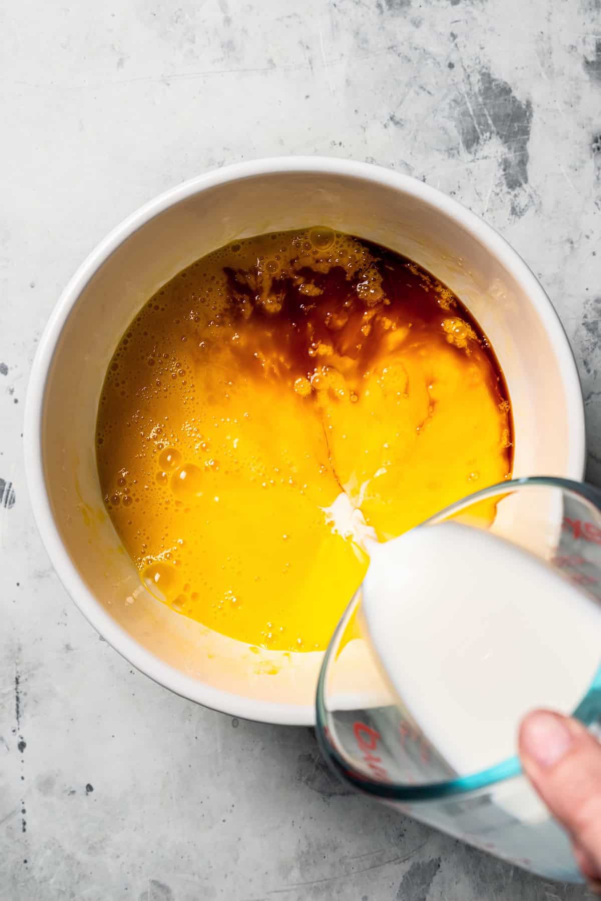 This German pancake recipe takes minutes to prepare and bakes up super soft, puffed, and golden in the oven. Made with only 6 ingredients! Milk being poured into a bowl of beaten eggs with vanilla.