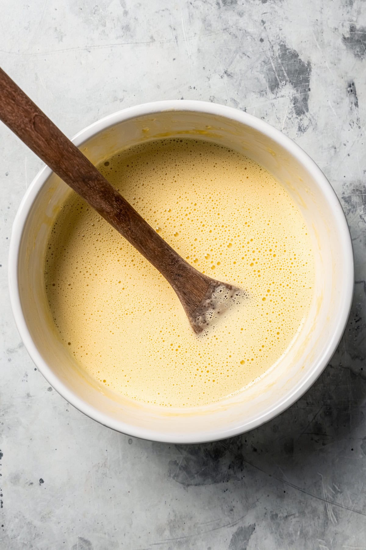 This German pancake recipe takes minutes to prepare and bakes up super soft, puffed, and golden in the oven. Made with only 6 ingredients! A wooden spoon resting in a bowl of pancake batter.