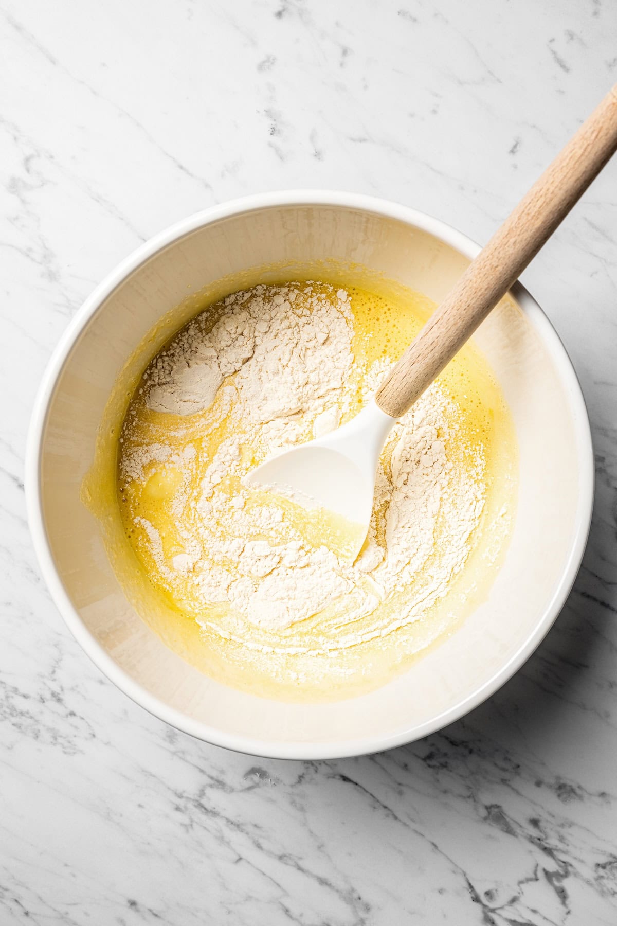 This authentic Mexican tres leches cake is a light, spongy cake soaked in a sweet milk mixture and topped with fluffy homemade whipped cream. Dry ingredients partially mixed into wet cake batter in a bowl.