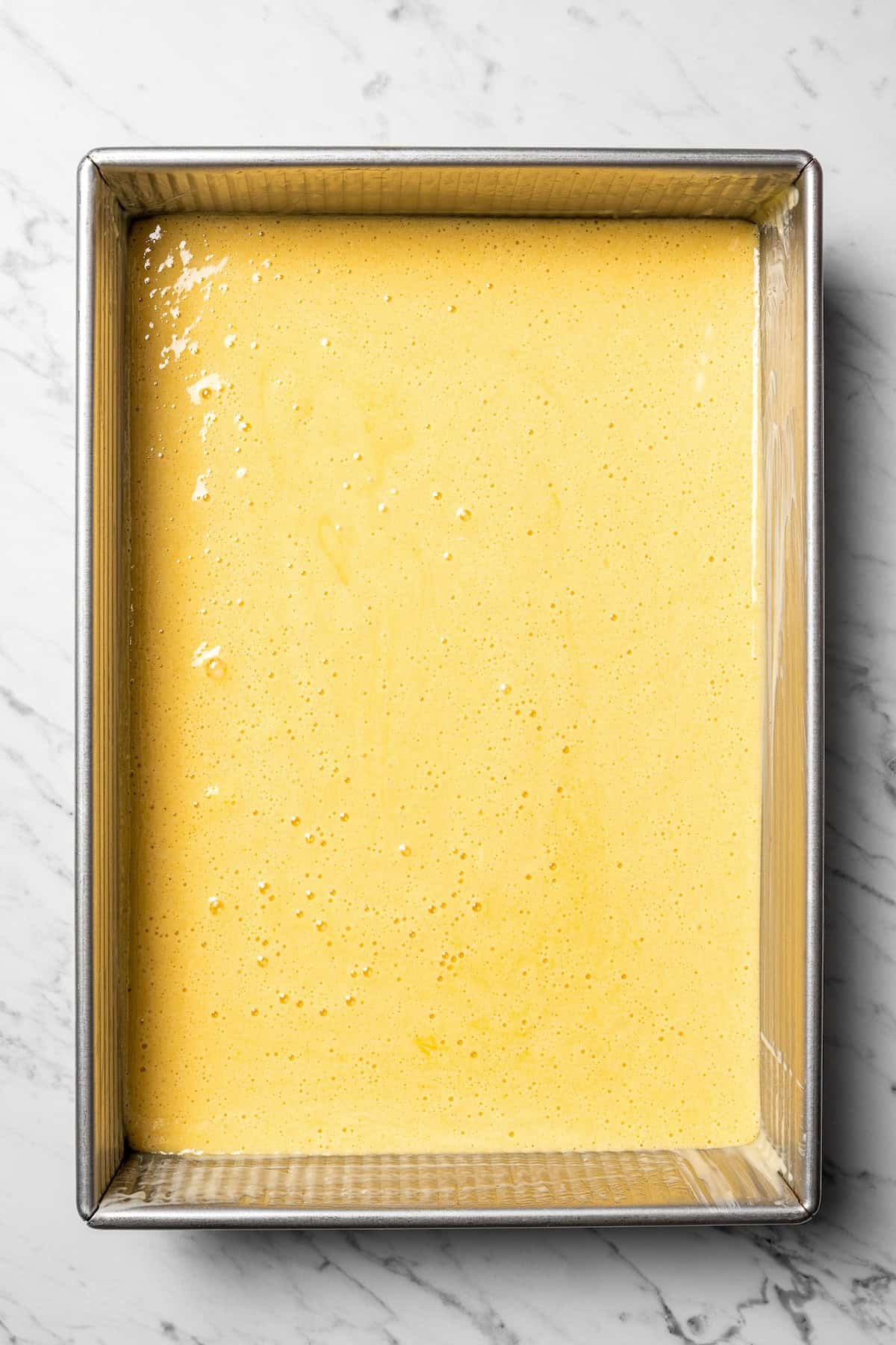 This authentic Mexican tres leches cake is a light, spongy cake soaked in a sweet milk mixture and topped with fluffy homemade whipped cream. Cake batter in a large rectangular baking pan.