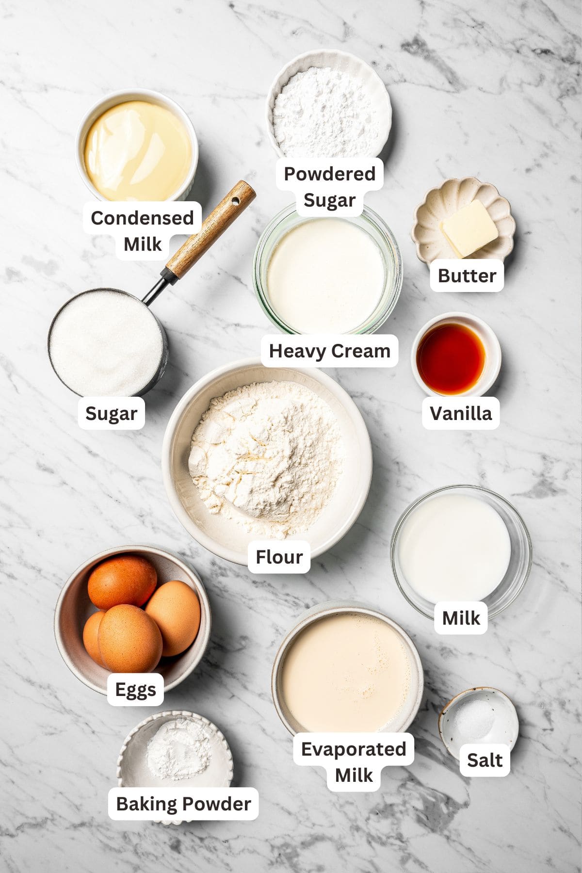 This authentic Mexican tres leches cake is a light, spongy cake soaked in a sweet milk mixture and topped with fluffy homemade whipped cream. Tres leches cake ingredients with text labels overlaying each ingredient.