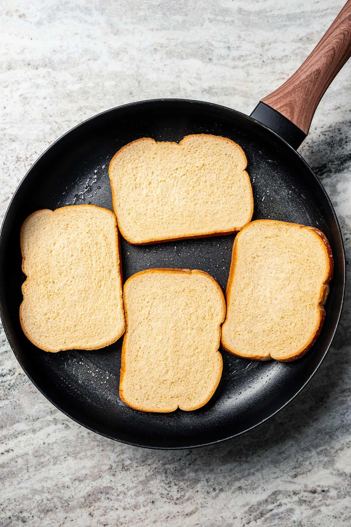 Four bread slices added to a skillet with melted butter.