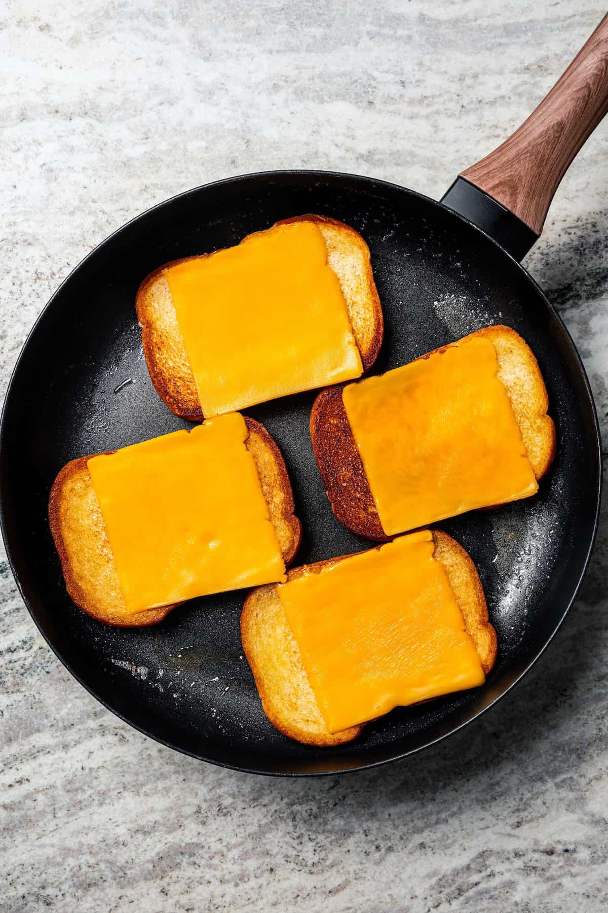 Four bread slices topped with American cheese toasting in a skillet.