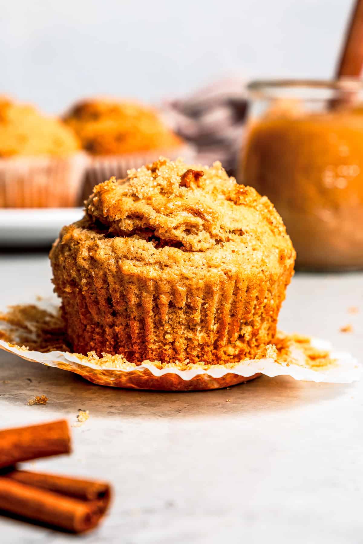 These moist applesauce muffins are easy to make and are packed with brown sugar and cinnamon, topped with extra sugar for a crunchy finish! An applesauce muffin unwrapped with a jar of applesauce and more muffins in the background.
