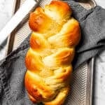 Baked challah next to a bread knife on a baking sheet lined with a dishcloth.