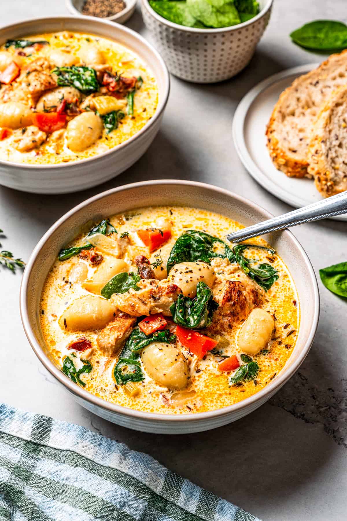 This chicken gnocchi soup is even better than the Olive Garden! It's ready in 20 minutes, extra creamy, and packed with flavorful ingredients. A spoon resting in a bowl of creamy chicken gnocchi soup, with a second bowl of soup and a plate of bread in the background.