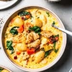 A bowl of gnocchi soup next to a plate of bread and a small bowl of spinach.
