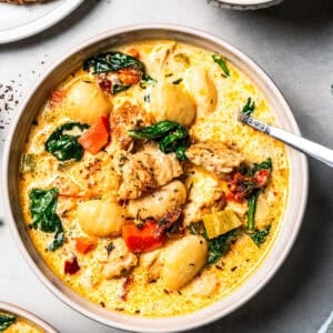 A bowl of gnocchi soup next to a plate of bread and a small bowl of spinach.