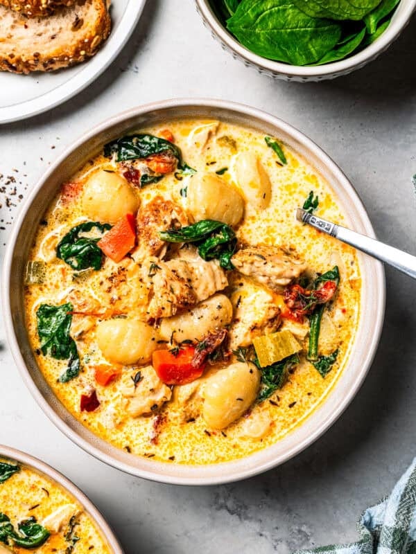 A bowl of gnocchi soup next to a plate of bread and a small bowl of spinach.