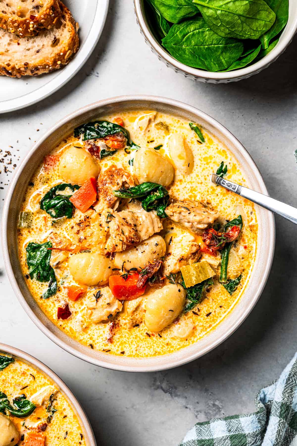 This chicken gnocchi soup is even better than the Olive Garden! It's ready in 20 minutes, extra creamy, and packed with flavorful ingredients. A bowl of gnocchi soup next to a plate of bread and a small bowl of spinach.