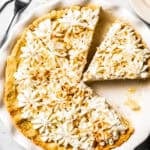 Coconut cream pie in a pie plate with one slice cut and a second slice missing.