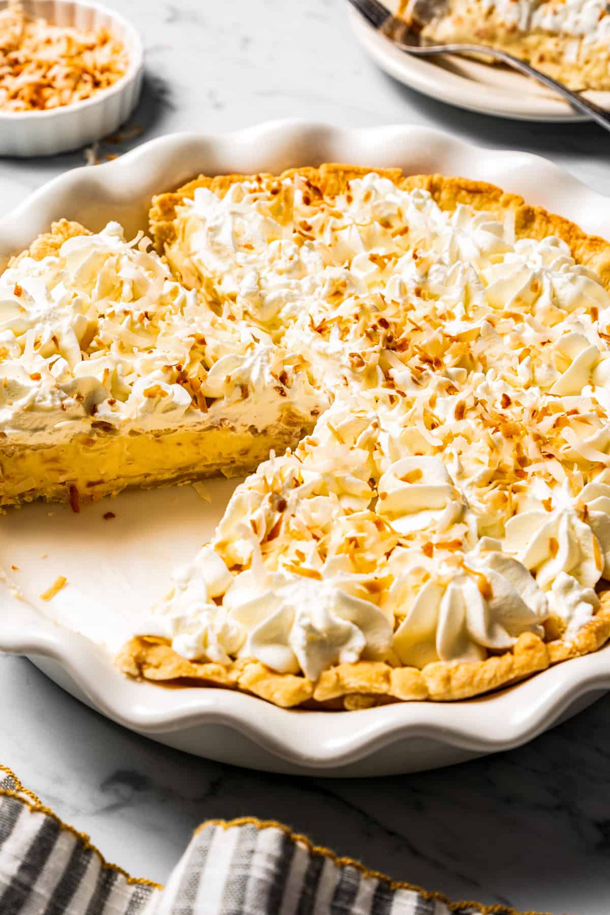 This easy coconut cream pie recipe features a thick, creamy coconut filling topped with fresh whipped cream in a golden, flaky pie crust. Sliced coconut cream pie in a dish.