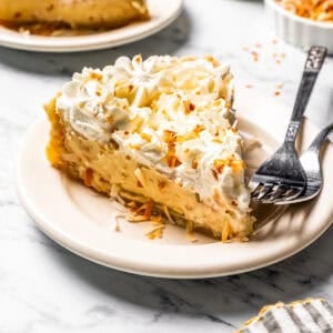 A slice of coconut cream pie on a plate with a second slice in the background.