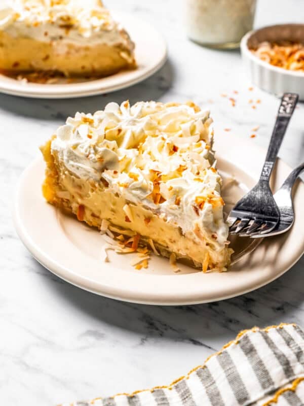 A slice of coconut cream pie on a plate with a second slice in the background.