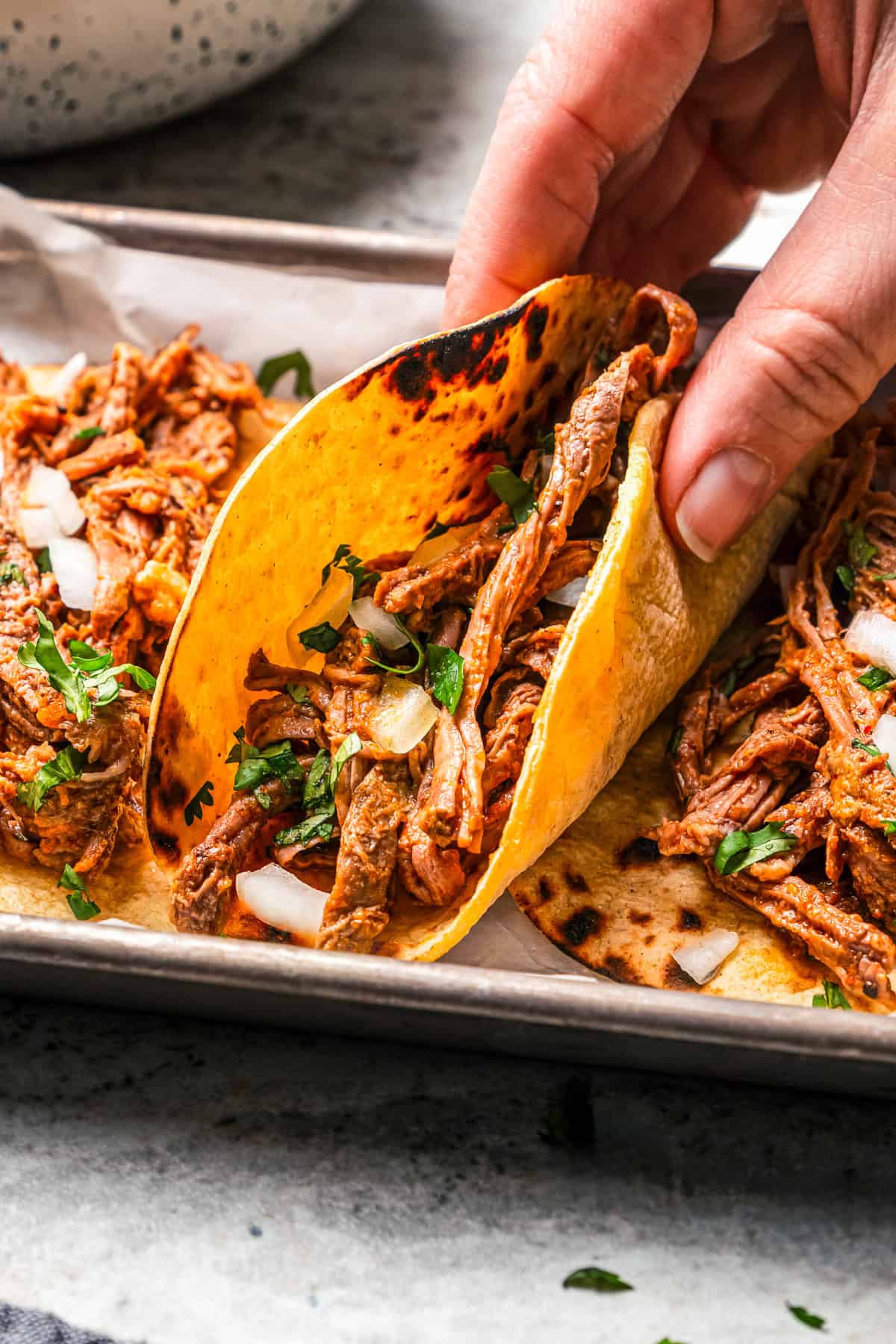 Crock pot carne asada has smoky spices and bright citrus, soaked into juicy shredded steak. Only 5 minutes to prep and perfect for tacos! A hand lifting a carne asada taco from a platter of tacos.