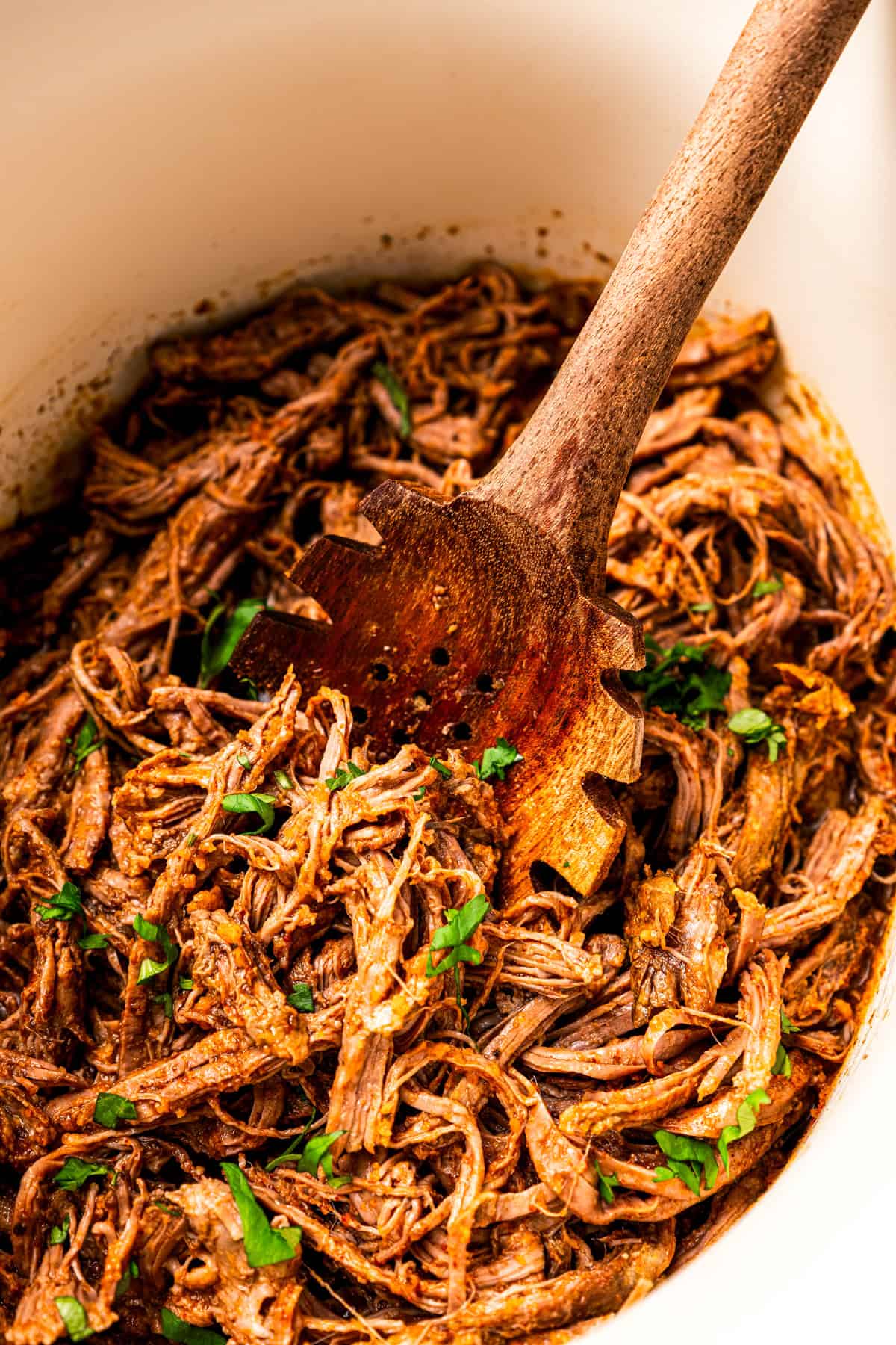Crock pot carne asada has smoky spices and bright citrus, soaked into juicy shredded steak. Only 5 minutes to prep and perfect for tacos! A wooden spoon resting in a crock pot of shredded carne asada.