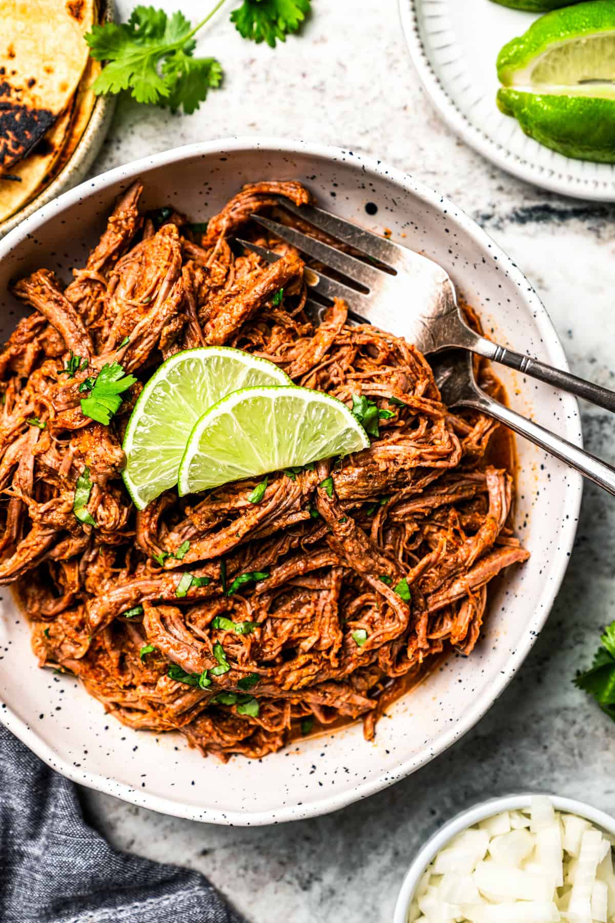Crock pot carne asada has smoky spices and bright citrus, soaked into juicy shredded steak. Only 5 minutes to prep and perfect for tacos! Shredded carne asada served in a bowl, garnished with lime wedges.