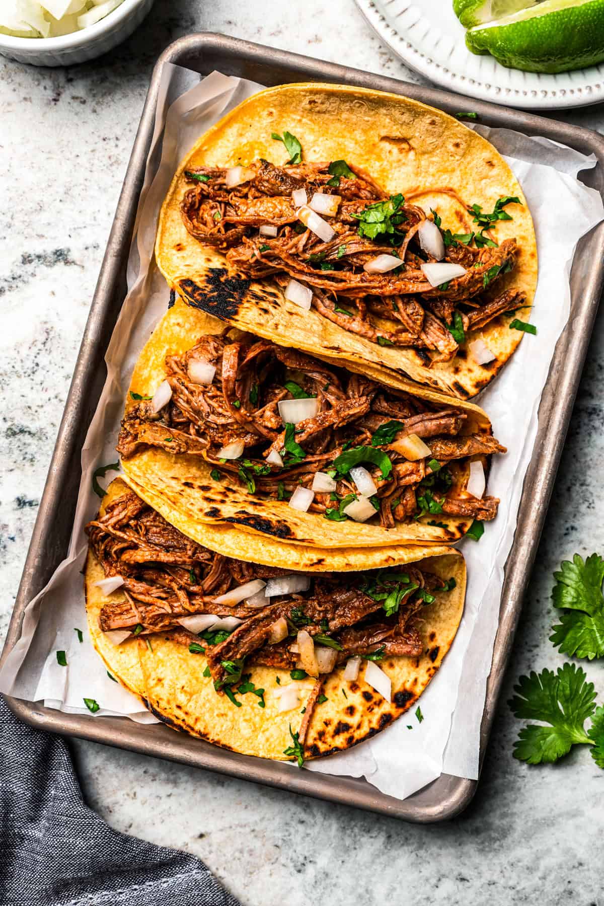 Crock pot carne asada has smoky spices and bright citrus, soaked into juicy shredded steak. Only 5 minutes to prep and perfect for tacos! Carne asada tacos arranged in a pan.