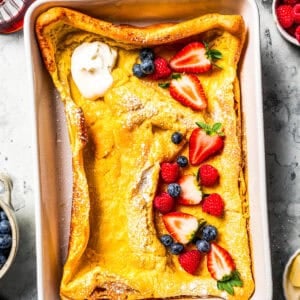 German pancake in a baking dish, topped with yogurt, fresh berries, and powdered sugar.