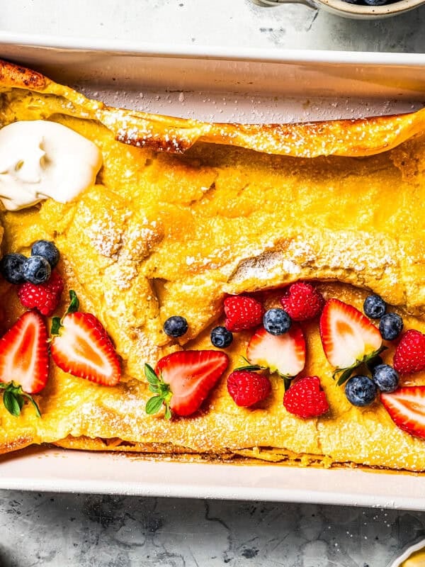 German pancake in a baking dish, topped with yogurt, fresh berries, and powdered sugar.