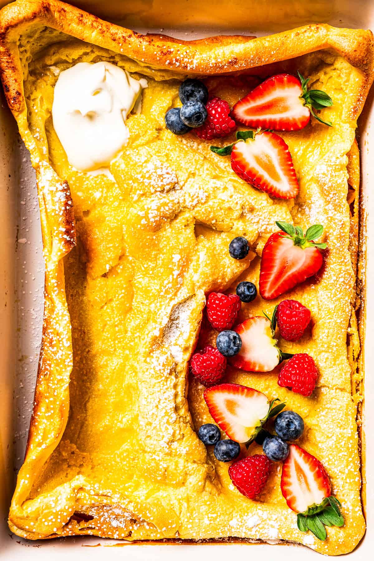 German pancake topped with yogurt, fresh berries, and powdered sugar.