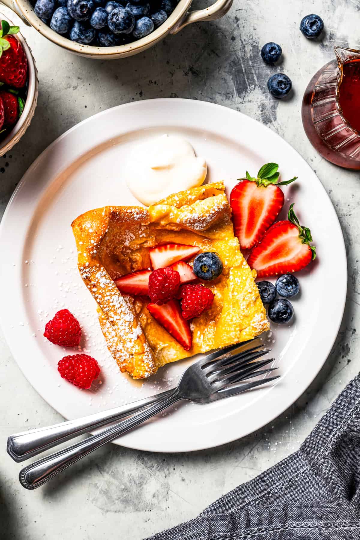 Overhead view of a German pancake slice garnished with fresh berries and powdered sugar on a plate with a fork.