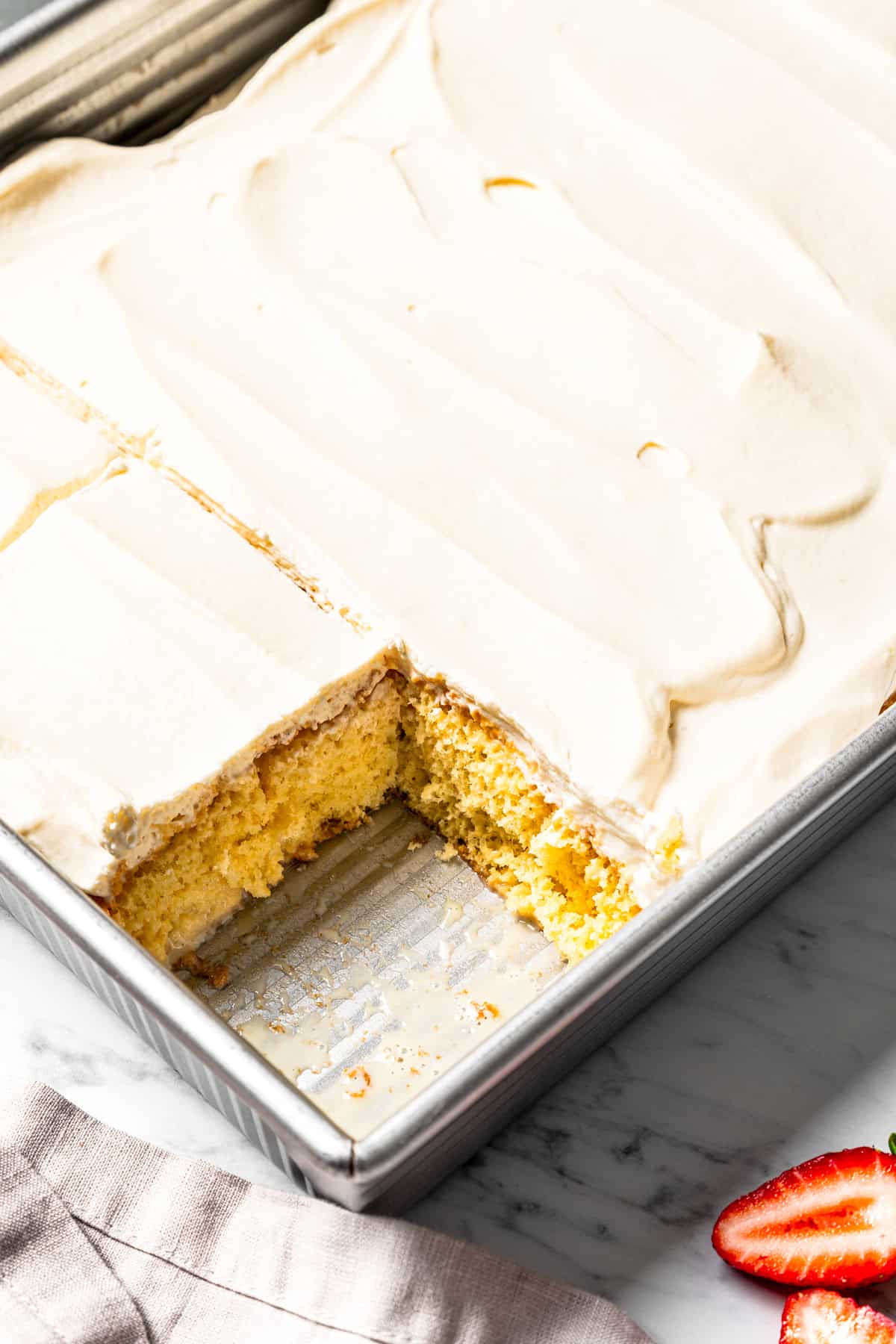 This authentic Mexican tres leches cake is a light, spongy cake soaked in a sweet milk mixture and topped with fluffy homemade whipped cream. Tres leches cake in a baking pan with a slice missing from the corner.