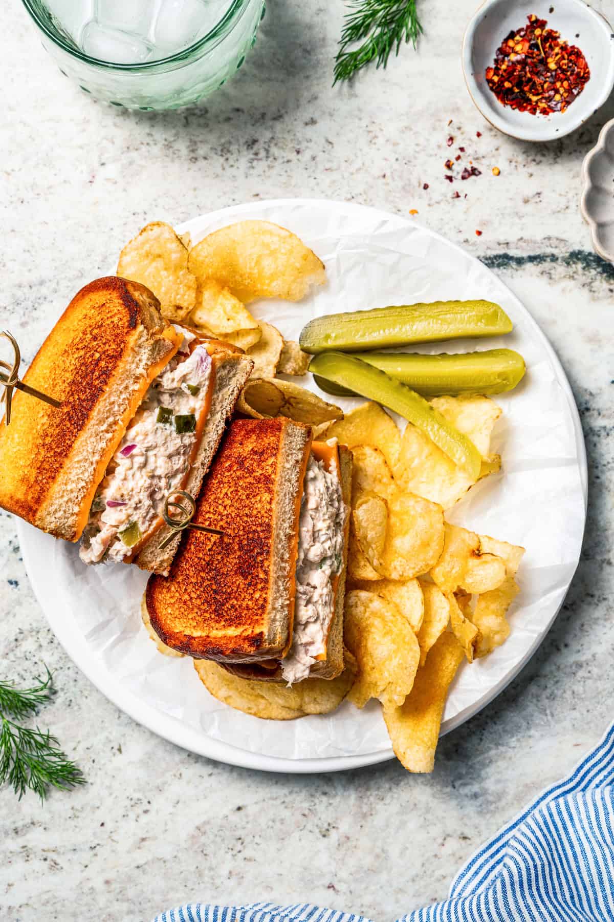 Tuna melt sandwiches served with pickles and potato chips on a plate.