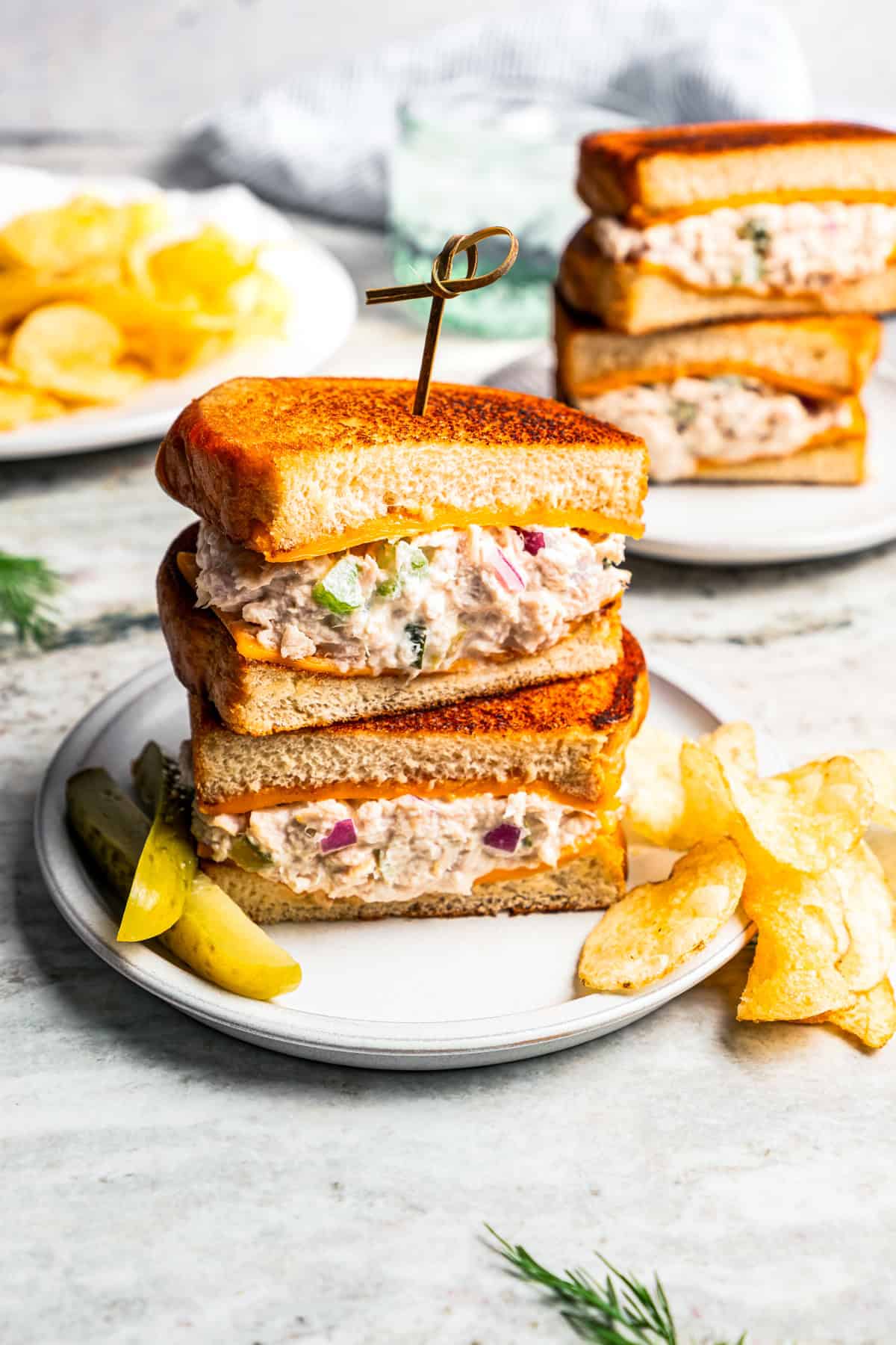 Tuna melt sandwich on a plate served with pickle spears and potato chips.