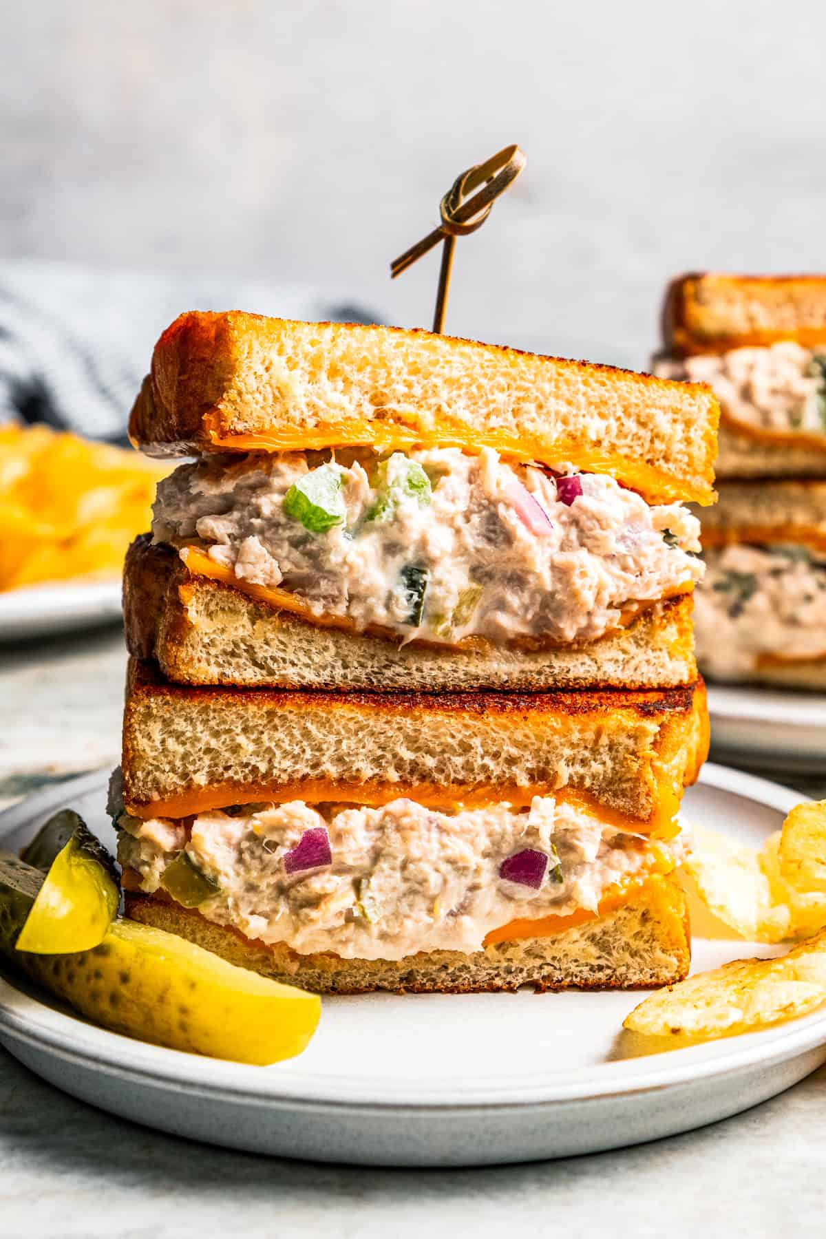 Two halves of a tuna melt stacked on a plate next to pickle spears.