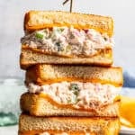 Three halves of a tuna melt stacked on a plate next to pickle spears.