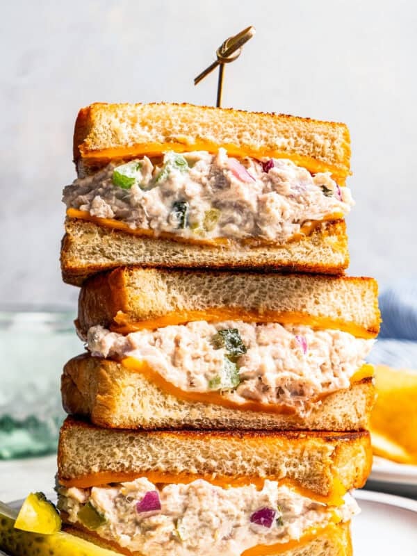 Three halves of a tuna melt stacked on a plate next to pickle spears.