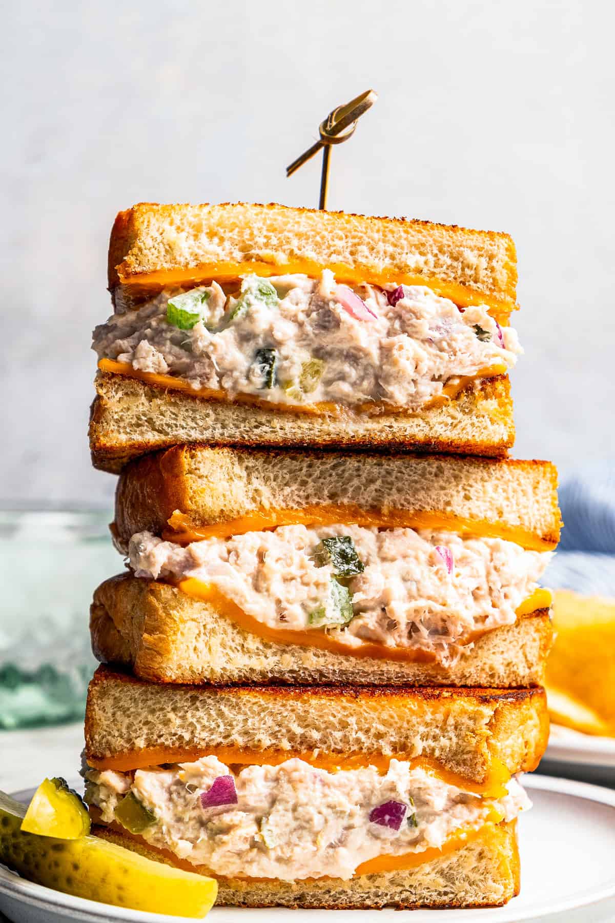 Three halves of a tuna melt stacked on a plate next to pickle spears.